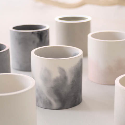 Concrete vessels in various colors - grey and white, pink and white, beige colors - on a subdued white background