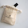 Makaka Perfume on white marble peeking out of the top of a muslin pouch with the name Makana stamped on it