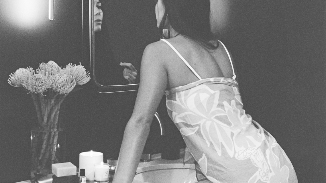 woman gazes into mirror, assorted Makana products in foreground