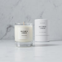 A Makana - Balsam & Cinder - Petite Candle with a glass container next to it, boasting soy wax for a fragrant experience.